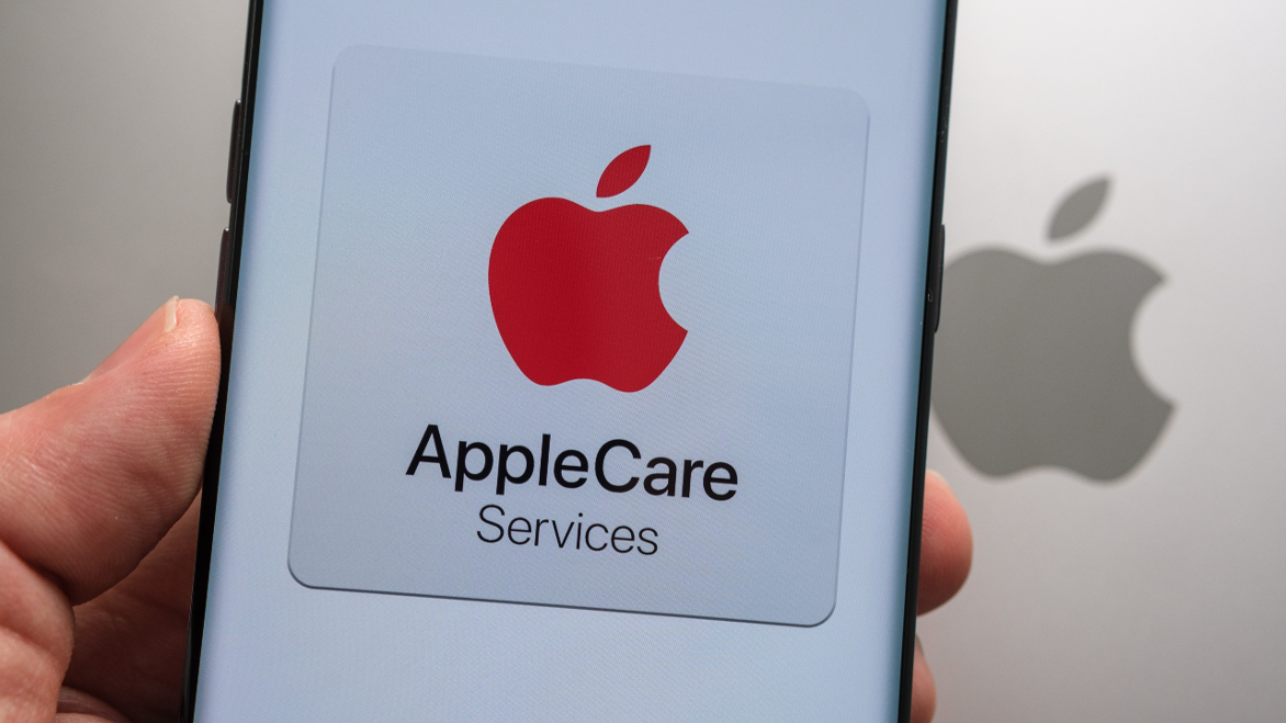 Apple Care Services logo seen on smartphone hold in a hand above the top of macbook with blurred apple logo.